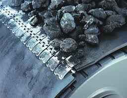 A conveyor belt carrying lump coal over its pulley, its two ends joined by a row of metal plate fasteners. A conveyor belt carrying lump coal over its pulley, its two ends joined by a row of metal plate fasteners.