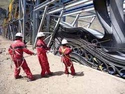 Three fitters in red overalls and hard hats pulling a new belt into a conveyor structure. Three fitters in red overalls and hard hats pulling a new belt into a conveyor structure.