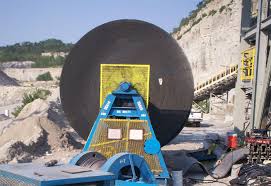 A large belt roll standing on a handling frame at a quarry, with the conveyor it is being fitted to behind it. A large belt roll standing on a handling frame at a quarry, with the conveyor it is being fitted to behind it.