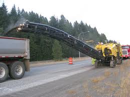 A road milling machine discharging asphalt into a tipper truck over its conveyor. A road milling machine discharging asphalt into a tipper truck over its conveyor.