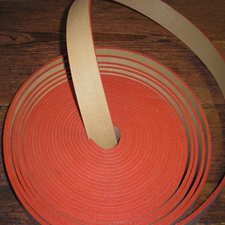 A coil of red rubber transmission belting with one end lifted away from the roll.