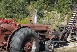 A farm tractor parked beside a machine it drives by a long flat belt.