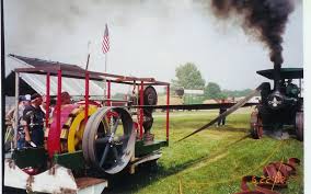 A traction engine driving a machine across a field by a flat belt.