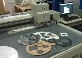 A cutting table with gaskets being cut from rubber sheet under a computer controlled head.