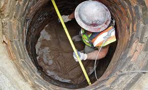 A worker in a harness and hard hat lining the inside of a manhole shaft.