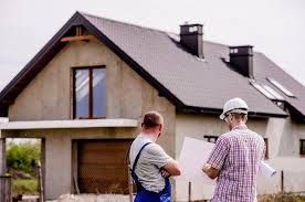 Two men on a building site holding insulation sheet against the wall of a house.
