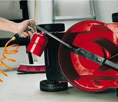 A hand holding an air gun connected to a coiled air line by a quick coupling, beside a red hose reel. A hand holding an air gun connected to a coiled air line by a quick coupling, beside a red hose reel.