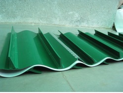 A green PVC belt with tall V cleats moulded across it, laid out on a floor.