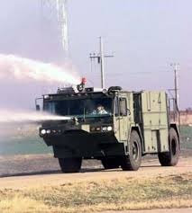 An airfield fire vehicle on open ground, spraying from its roof monitor.